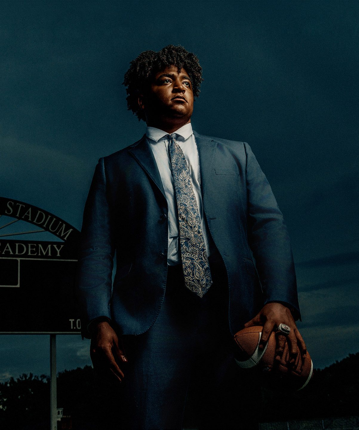 Delaware senior portrait photographer | Image of a football player in a suit, holding a football and showcasing his championship ring.