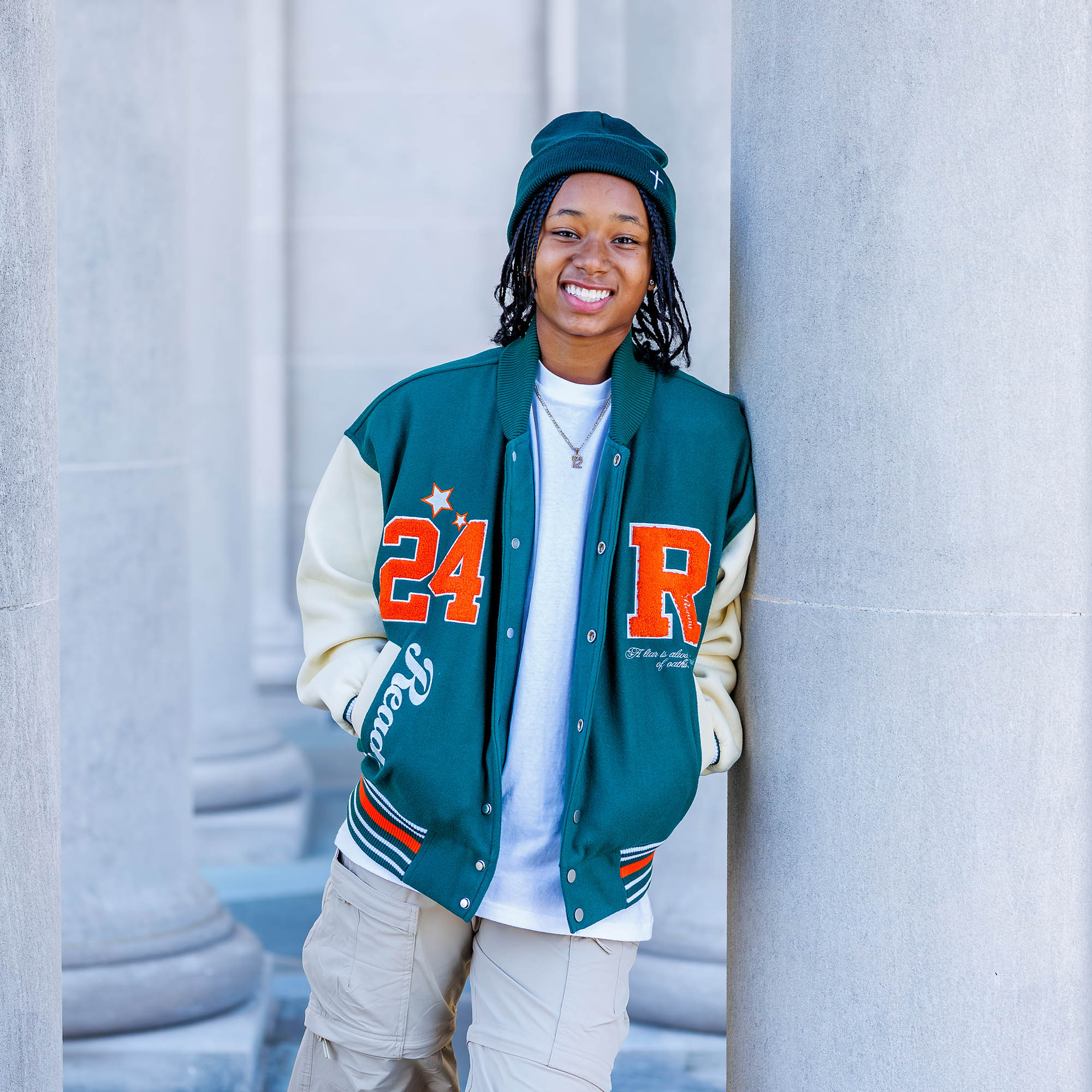 Delaware Senior Portrait Photographer | A female dressed in a stylish letter jacket, flanked by white pillars poses outdoors in a park.